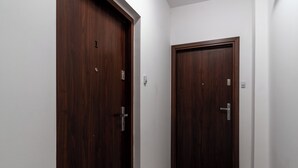 A hallway with two wooden doors, a doormat, and a light switch on the wall. - Silesian Charm Kozielska 1 Studio (Katowice)