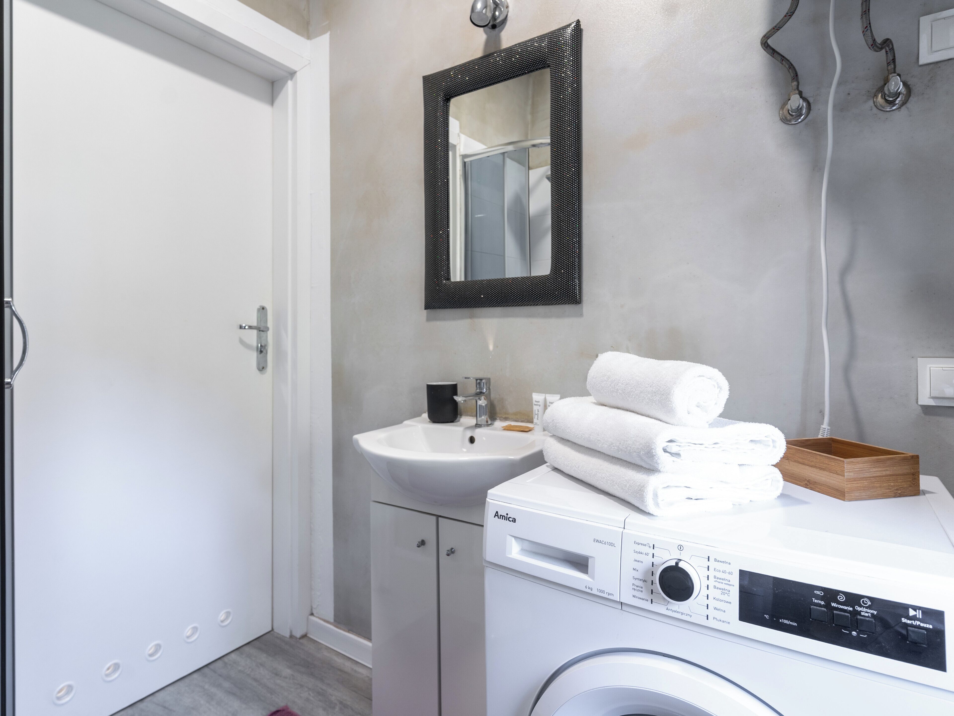 A modern bathroom with a white sink, a mirror, a washing machine, and a wooden tray.