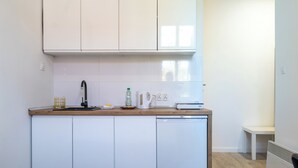 Eine kompakte Küche mit weißen Schränken, einer Holz Arbeitsplatte, einer Spüle, einem Wasserkocher und einem Geschirrspüler.