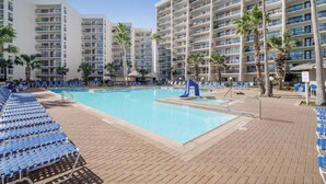 A hotel pool area with multiple levels of balconies, palm trees, and blue lounge chairs.