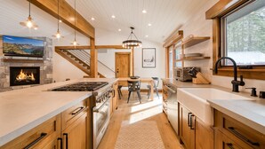 A modern kitchen with a stone fireplace, wooden beams, a large island, and a dining area.