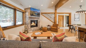 A cozy living room with a stone fireplace, a large window, and a staircase leading to another level.
