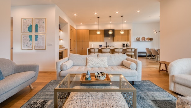 A modern living room with a sofa, coffee table, and a dining area with chairs and a kitchen in the background.