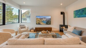 A modern living room with a large window, a fireplace, a sofa, and a television displaying a scenic landscape.