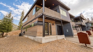 A modern two-story house with a balcony, large windows, and a view of the surrounding landscape.