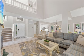 A spacious living room with a high ceiling, a staircase, a sofa set, and a dining area.