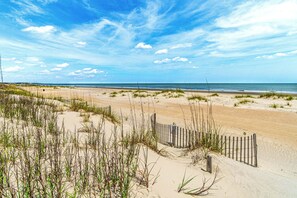 A beach with sand dunes, a wooden fence, and the ocean in the background.