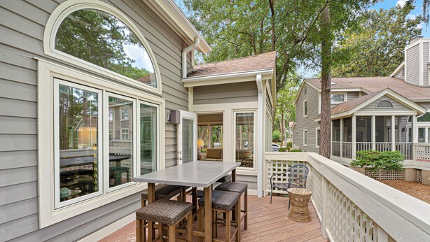 A deck with a table and chairs, a wooden fence, and a house with large windows. - Family Villa | Deck, Lagoon Views, Complex Pool, Bikes (Hilton Head Island)
