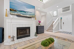 A spacious living room with a fireplace, a large flat-screen TV mounted above it, a staircase leading to another level, and a door with a sign.