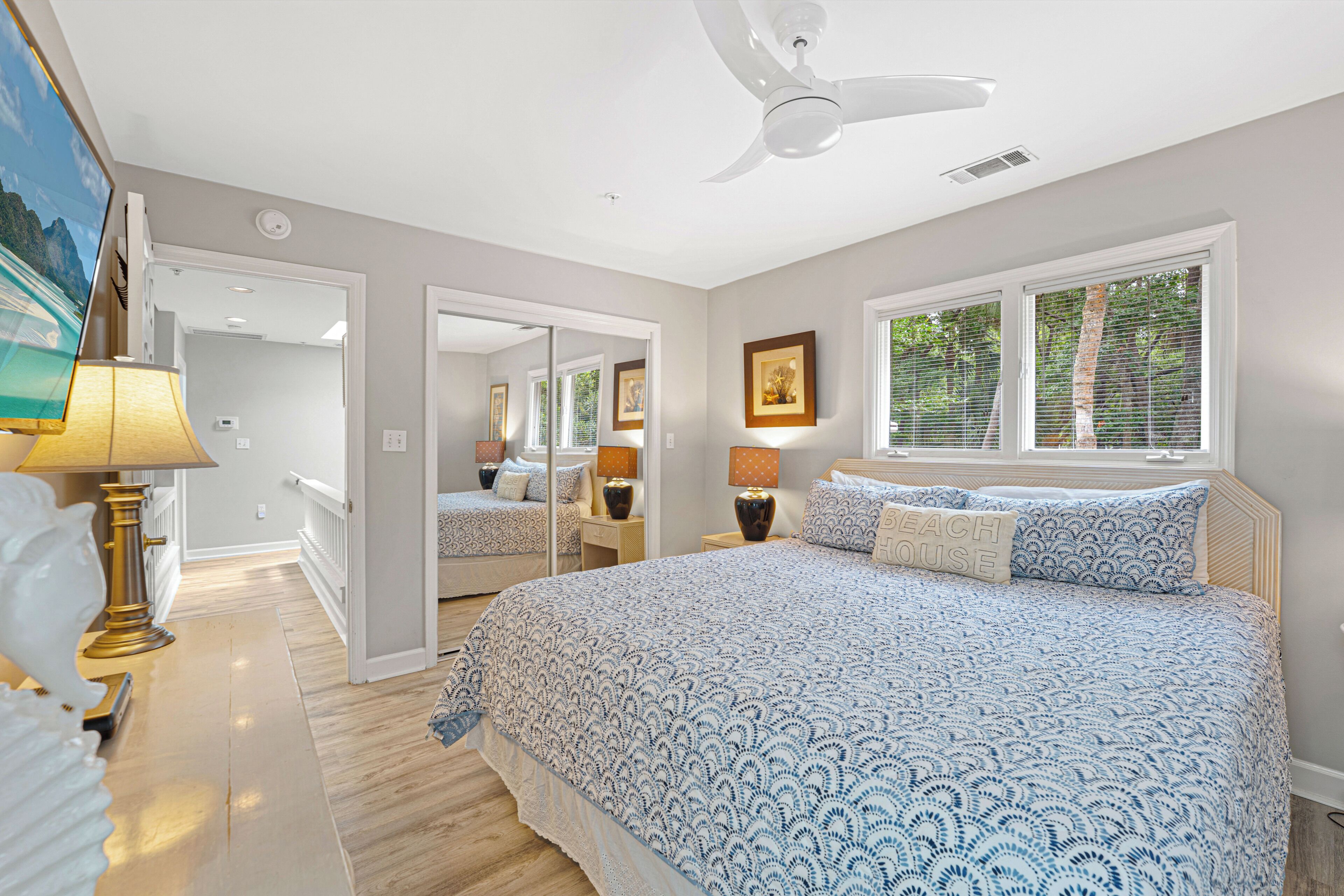 Une chambre avec un grand lit, un ventilateur de plafond et une vue sur l’extérieur par la fenêtre.