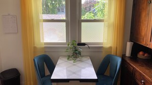 Een eetgedeelte met een tafel en twee stoelen, een kamerplant, een agenda en een raam met gordijnen.