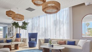 Un salon moderne avec un canapé bleu, une table basse ronde et une grande fenêtre ornée de rideaux légers.