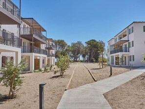 A modern apartment complex with multiple balconies, a sandy courtyard, and a clear blue sky.