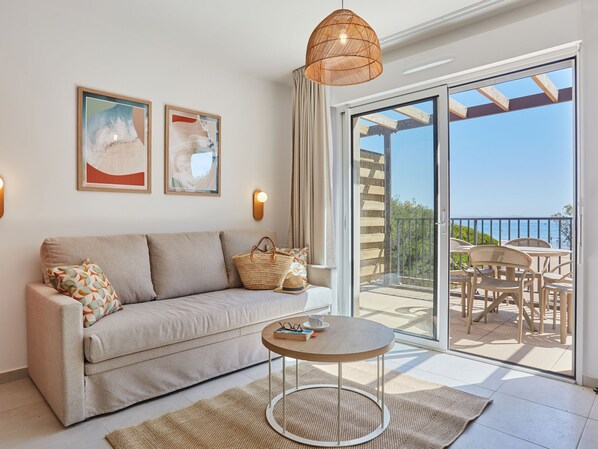 A modern living room with a sofa, a round coffee table, and a view of the outside balcony.