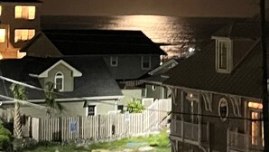 Vista nocturna de una zona residencial con casas y un cuerpo de agua al fondo.