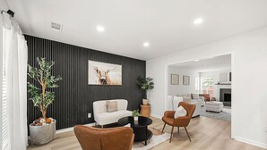 Een moderne woonkamer met een bank, salontafel en stoelen, een zwarte accentmuur en een haard op de achtergrond.