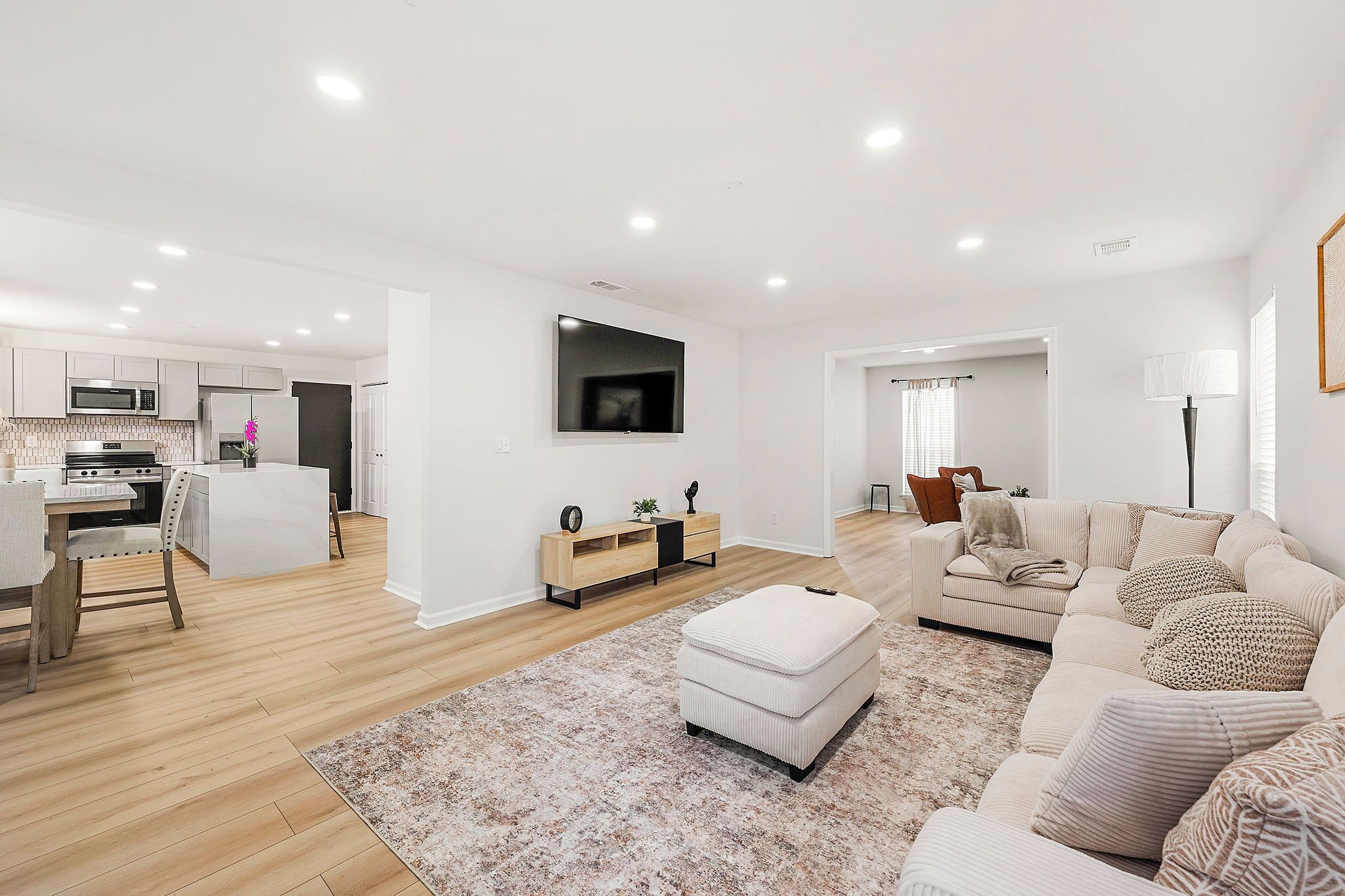 Un salon moderne avec un canapé, un pouf et un téléviseur à écran plat fixé au mur.
