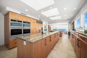 A modern kitchen with built-in ovens, a large island, and a view of the ocean. - Panoramic Ocean Views with Sauna, AC, and Parking (Long Beach)