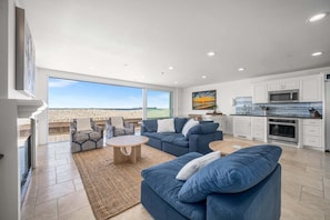 A spacious living area with a large window, a kitchen with white cabinets, and a view of the desert. - Panoramic Ocean Views with Sauna, AC, and Parking (Long Beach)