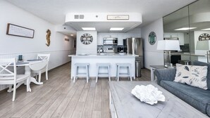 A modern kitchen with white cabinetry, a central island with stools, and a dining area with white chairs. - Luxe Gulf-front Free Beach Chairs Balcony View Resort Amenities ON THE Beach (Panama City Beach)