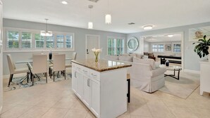 A modern kitchen with a central island, dining area with chairs, and a living area with a sofa and coffee table. - Barefoot In Lantana Paradise (Lantana)