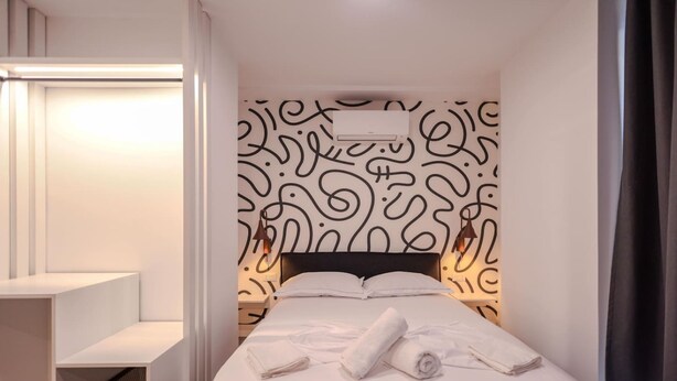 A modern hotel room with a neatly made bed, a bedside table, and a wall with a decorative pattern. - Grandstay Studio 110 (Durrës)