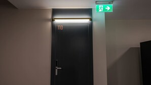 A dark-colored door with the number 110, an emergency exit sign above it, and a light strip above the door. - Grandstay Studio 110 (Durrës)