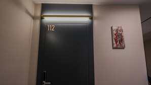 A black door with the number 112, a light strip above it, and a piece of abstract art on the wall. - Grandstay Studio 112 (Durrës)