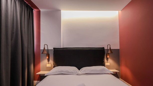 A hotel room with a bed, two bedside lamps, a nightstand, and a curtain. - Grandstay Studio 112 (Durrës)