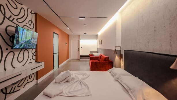 Ein modernes Hotelzimmer mit einem großen Bett, einem an der Wand befestigten Fernseher, einem roten Sofa und einem kleinen Tisch.