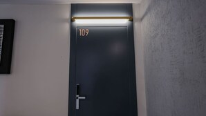 Eine dunkel gefärbte Tür mit der Nummer 109, eine Leuchte darüber und eine strukturierte Wand zur Rechten.