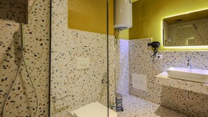 Ein Badezimmer mit einem weißen Waschbecken, einem Spiegel und einer Duschkabine mit Glastür.