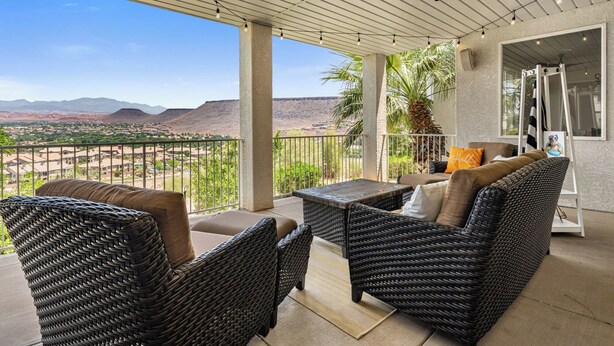 Un patio techado con muebles de mimbre, vistas a un paisaje desértico y una piscina visible a través de puertas de vidrio.