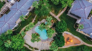 Vista aérea de una zona residencial con piscina, sillas de descanso y un pequeño parque infantil.
