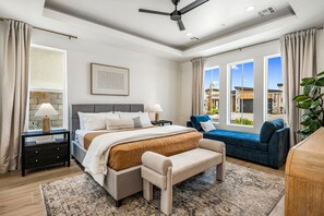 Un dormitorio moderno con cama, mesitas de noche, un banco, un sofá y un amplio ventanal con vistas.