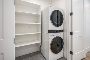 Una sala de lavandería con dos lavadoras apiladas, un estante blanco y una puerta.