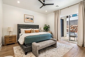 Un dormitorio con cama, mesita de noche, lámpara y vistas al exterior.