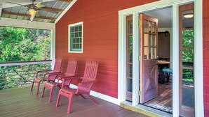 Un portico di legno rosso con tre poltrone Adirondack, una ventola a soffitto e una porta scorrevole in vetro che dà su un'area pranzo interna.