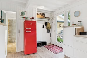 A compact kitchen with a red refrigerator, wooden cabinets, a small sink, and a window with a view of greenery.