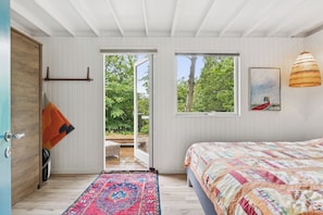 Quarto com cama, janela, porta e vista para o verde lá fora.