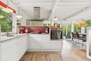 A modern kitchen with white cabinets, a red kettle, and a large window.