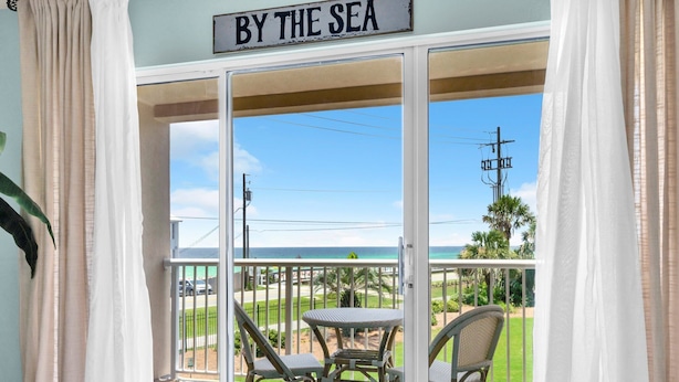 A balcony with a view of the sea, a table, and two chairs.