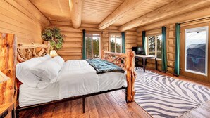 A wooden cabin bedroom with a bed, a wooden headboard, a window, and a view of the outdoors.