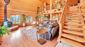 A spacious log cabin interior with a wooden staircase, a large sofa, and a fireplace.