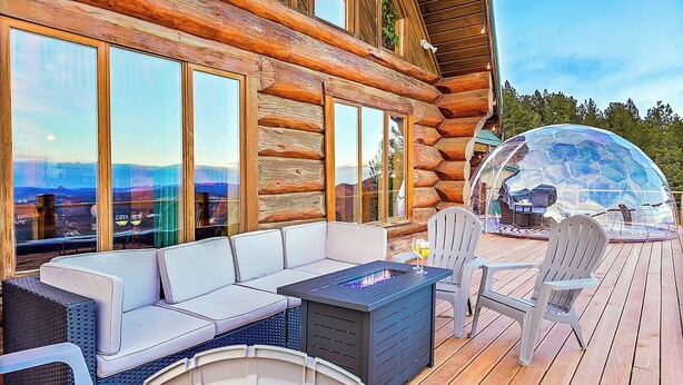 A log cabin with a deck featuring a sofa, chairs, and a fire pit.
