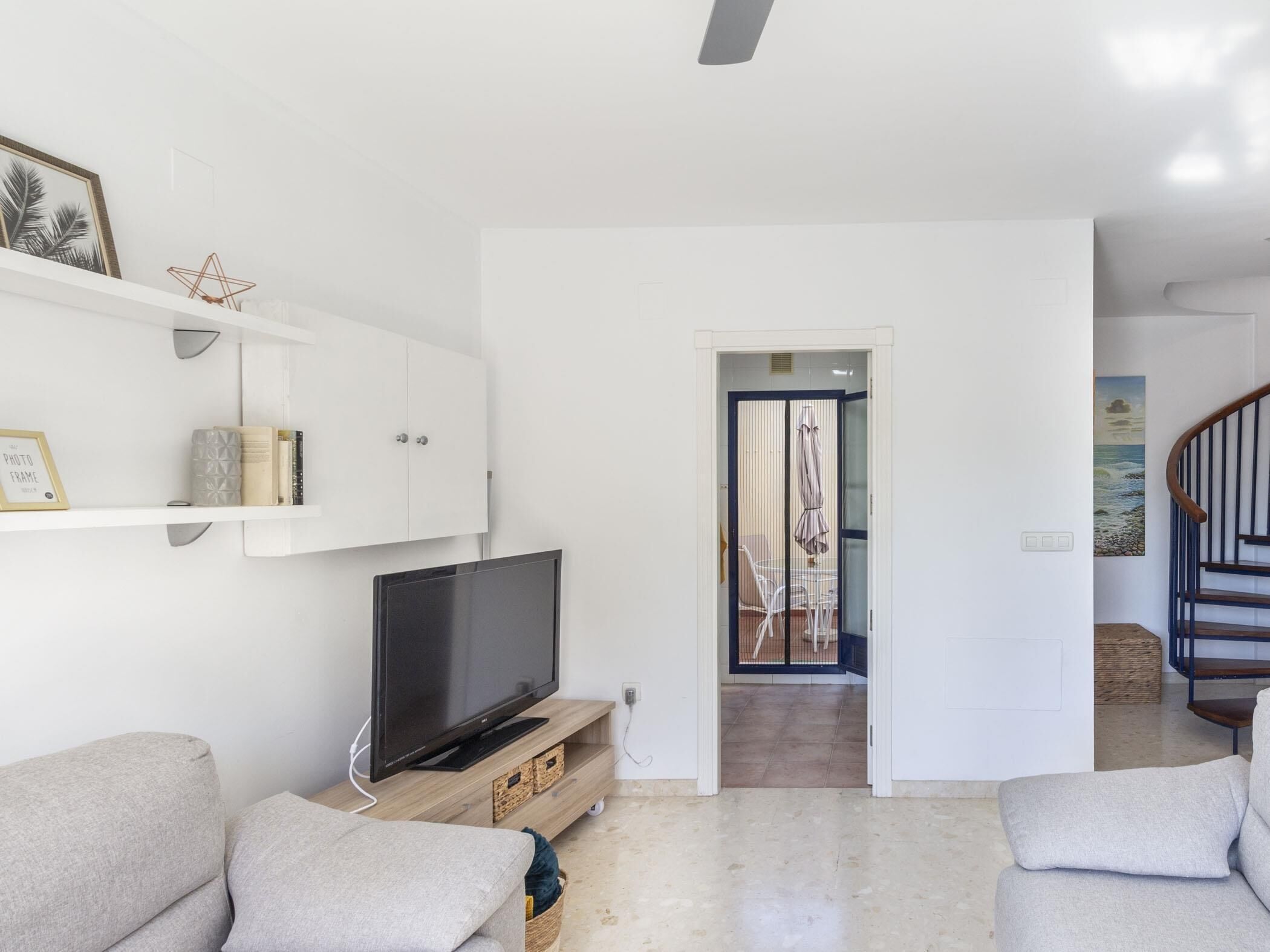 A modern living room with a flat-screen TV on a wooden stand, a sofa, and a cabinet with decorative items.