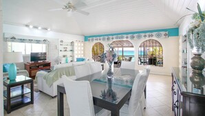 A spacious living room with a dining area, a ceiling fan, and a view of the ocean.