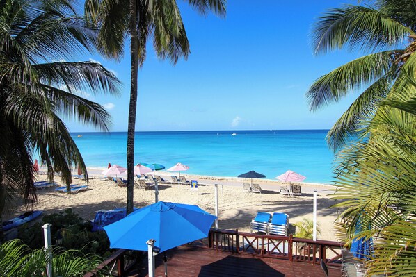 Une plage avec une eau d’un bleu limpide, des palmiers et des chaises de plage sous des parasols.