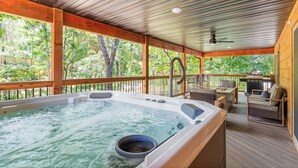 A hot tub area with a view of trees, a ceiling fan, and a barbecue grill.