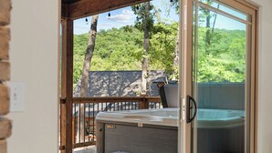 Een hottub op een houten terras met een glazen deur die uitkomt op een weelderig groen landschap.